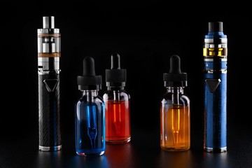 Electronic cigarettes and bottles with vape liquid on black background