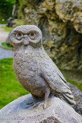 Old owl sculpture on stone in a park or garden.