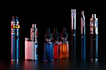 Electronic cigarettes and bottles with vape liquid on black background. Toned light