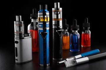 Electronic cigarettes and bottles with vape liquid on black background