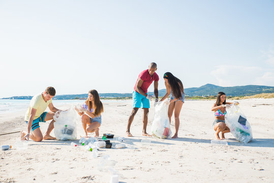 Group Of Activists Friends Collecting Plastic Waste On The Beach. People Cleaning The Beach Up, With Bags. Concept About Environmental Conservation And Ocean Pollution Problems