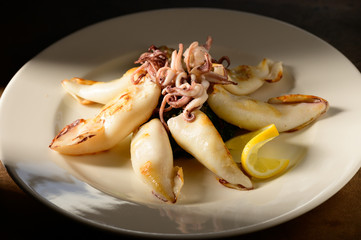 Grilled Calamari (Squid) with lemon and parsley on white plate on a plate in restaurant ready to be served