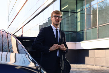 Handsome serious young businessman standing near his comfortable new car and going to the office.