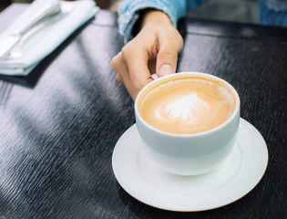 White Cup of cappuccino coffee with foam on the table in a cafe or restaurant with a shiny spoon in a woman`s hand