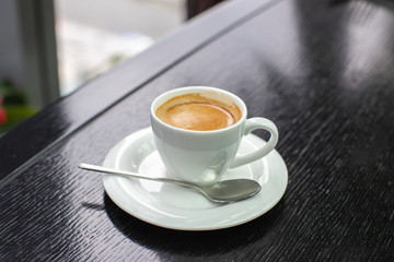 white Cup of cappuccino or expresso coffee with foam on the table in a cafe or restaurant with a shiny spoon