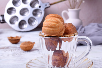 Walnut shaped cookies with caramel in a glass cup on the white table. Special skillet in the background