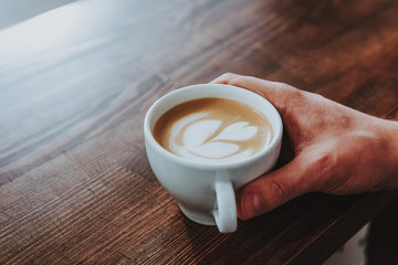 Close up of hand holding cup of coffee with latte art