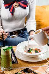 Beautiful serving of vegetable broth in the restaurant. Bouillon is poured from a white teapot into a white plate of vegetables. Girl eating soup in a restaurant. close up