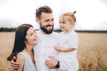happy family on the walk in the wheat field: stylish bearded man and a cute young wife with her little daughter happy parents with her baby.  selective focus