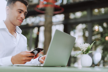 Handsome young man with cellphone using laptop in outdoor cafe