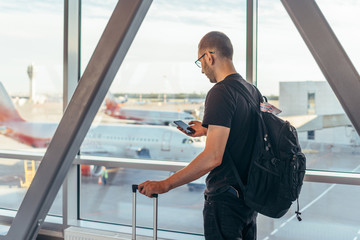 Young woman standing near window at airport holding mobile phone