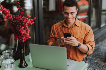 Handsome young man with modern laptop using cellphone