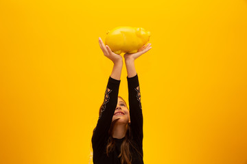 Caucasian little girl over isolated yellow background holding a big piggybank.