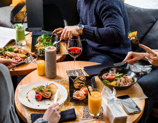 Lunch of three friends in a restaurant with salad with avocado, tomatoes, poached egg, beef, orange, arugula and roasted salmon fillet and risotto with cuttlefish. Close up. Top view.