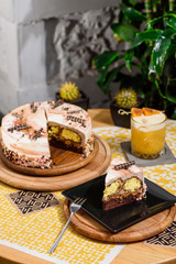 Fototapeta na wymiar Beautiful chocolate layered cake with yellow filling and beautiful coffee glaze, decorated with tubules and pastry beads. Cake on a beautiful yellow background on a wooden table in the restaurant