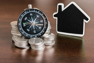 Stack of coins with compass and home shaped on wood table