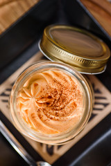 Coffee and traditional Italian dessert tiramisu in a jar on a wooden table in the restaurant. Beautiful pumpkin tiramisu serving in a restaurant on a yellow background. close up