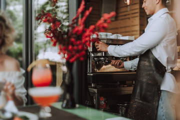 Smiling barman in black apron using professional coffee machine