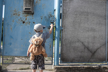 a little boy in the yard with a backpack near the gate