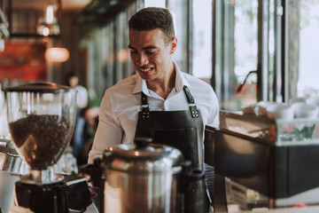 Handsome barman in black apron working in coffee shop