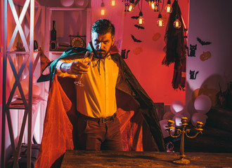 Fototapeta premium Halloween party. Magician drinks sparkling wine. Attractive bearded man in black magical coat. Halloween holiday concept.