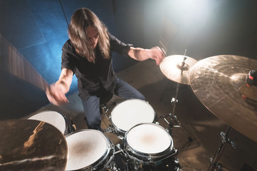 Portrait of a long-haired drummer with chopsticks in his hands sitting behind a drum set. Low key. Concepts of the creative freedom of the millenial generation