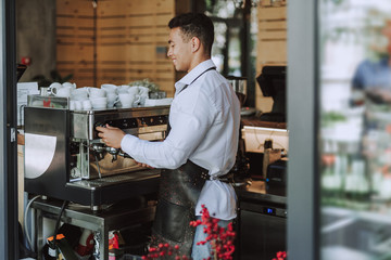 Smiling barman in black apron using professional coffee machine