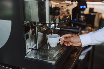 Young man using professional coffee machine to make fresh espresso