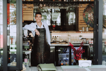 Handsome bartender in black apron standing in cafe