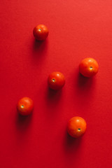 Five cherry tomatoes on a red background. Flat lay.