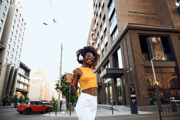 Happy afro-american woman with coffee dancing on the street