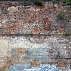 full frame image of a very large old brick wall with many patched and repaired sections stains weeds and faded painted areas