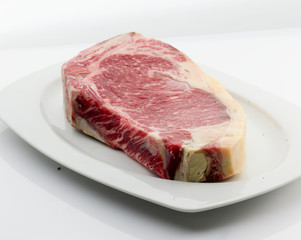  plato de porcelana blanca con Chuletón de vaca cruda y fresca. white porcelain plate with raw and fresh beef T-bone steak.