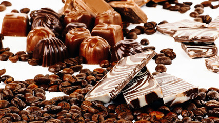 sweet chocolate candies and coffee beans on white background