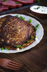 potato pancakes with green onions and sour cream on a dark wooden table, sliced pork and bacon