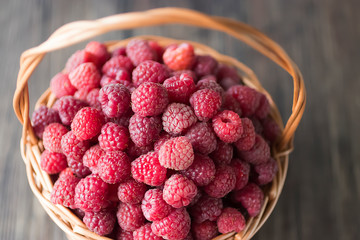 Fresh raspberries in brown basket on gray background.