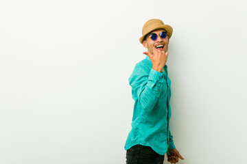 Young hispanic man wearing a summer clothes points with thumb finger away, laughing and carefree.