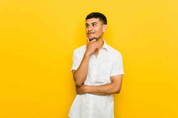 Young hispanic man looking sideways with doubtful and skeptical expression.