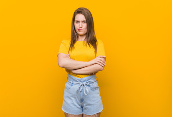 Young woman teenager wearing a yellow shirt frowning face in displeasure, keeps arms folded.