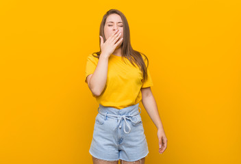 Young woman teenager wearing a yellow shirt yawning showing a tired gesture covering mouth with hand.