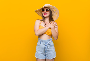 Young caucasian woman wearing a straw hat, summer look has friendly expression, pressing palm to chest. Love concept.