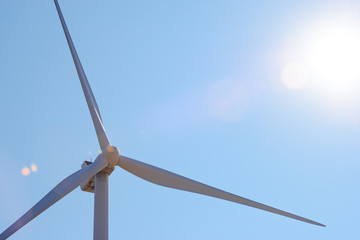 Wind Generator Turbine in Bright Sun Light on the Blue Sky Bacground. Green Renewable Energy Concept.