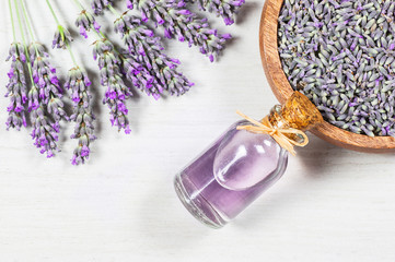 Glass bottle of Lavender essential oil with fresh lavender flowers and dried lavender seeds on white rustic table, aromatherapy spa massage concept. Lavendula oleum