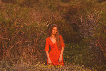 Young blonde girl in red dress staying among trees