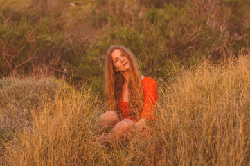 Young blonde girl in red dress sitting on grass