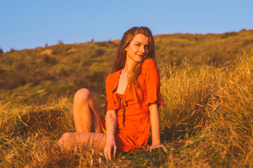 Young smiling blonde girl in red dress sitting on grass