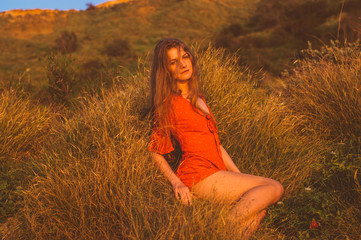 Young blonde girl in red dress sitting on grass