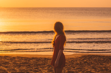 Young blonde girl in red dress staying in the evening on the beach