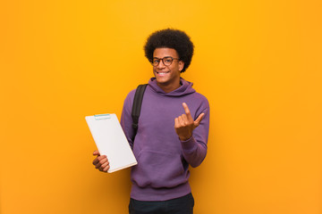 Young african american student man holding a clipboard inviting to come