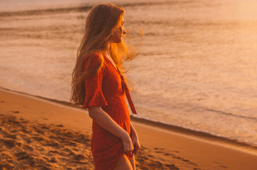 Young blonde girl in red dress staying in the evening on the beach